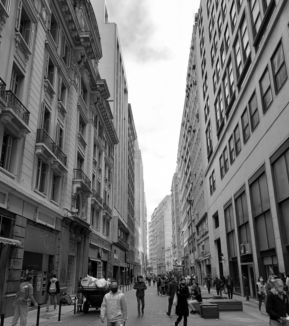 Rua sem árvores cercada por prédios. Foto em preto e branco